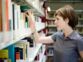 Kobieta, która wygląda jak bibliotekarz, wybiera książkę z półki w bibliotece.