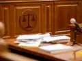 Sądowa sala z symbolem wagi sprawiedliwości i stosem dokumentów, zapewniająca zgodność z oryginałem.