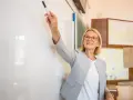 Nauczycielka z markerem przy tablicy, uśmiechnięta. To może być ocena pracy nauczyciela początkującego.