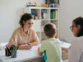 Uśmiechnięta nauczycielka omawia z rodzicami orzeczenie o potrzebie kształcenia specjalnego dla dziecka.