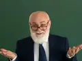 Uśmiechnięty starszy pan z brodą, w okularach i garniturze, gestykuluje, jakby wyjaśniał świadczenie kompensacyjne.