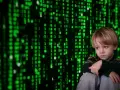 Smutny chłopiec siedzi przed ekranem z zielonym kodem, symbolizującym cyberprzemoc.