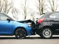 Wypadek drogowy. Niebieski i czarny samochód zderzyły się. To zdarzenie to siła wyższa, jakby kodeks pracy nie obowiązywał.
