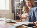 Praca na urlopie macierzyńskim? Młoda mama z dzieckiem przy biurku z laptopem i tabletem, pokazująca, że można łączyć obowiązki.
