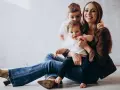 Szczęśliwa mama z dwójką dzieci, maluszkiem na rękach i starszym synkiem za plecami. Idealny urlop na dziecko.