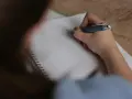 Uczeń pisze w zeszycie, zastanawiając się, ile trwa egzamin ósmoklasisty.