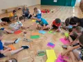 Dzieci klas 1-3 biorą udział w zabawach integracyjnych, rysując na kolorowych kartkach.