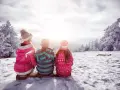Dzieci siedzą na ławce, podziwiając zimowy krajobraz. Słońce przebija się przez chmury, tworząc magiczną atmosferę podczas ferii zimowych.