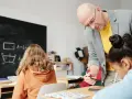 Nauczyciel pomaga uczniom podczas zajęć dydaktyczno wyrównawczych. Na tablicy wzory matematyczne.