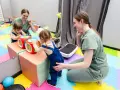 Dwie małe dziewczynki bawią się interaktywną kostką, a fizjoterapeutka wspiera ich rozwój. Www.