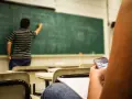 Nauczyciel pisze na tablicy, a uczeń w pierwszej ławce przegląda telefon. Obowiązki nauczyciela to nie tylko nauczanie, ale też pilnowanie porządku.