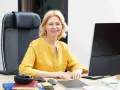 Uśmiechnięta wicedyrektor w okularach siedzi przy biurku, przed nią komputer i słuchawki.