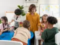 Nauczycielka podczas kursu opiekuna w żłobku pomaga dzieciom w zabawie klockami i sorterem.