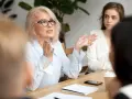 Kobieta w okularach gestykuluje, prowadząc dyskusję podczas rady pedagogicznej.