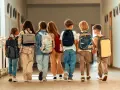 Siedmioro dzieci z plecakami idzie korytarzem szkolnym, ciesząc się ostatnimi dniami wolnymi od szkoły.