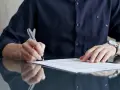 Mężczyzna w granatowej koszuli podpisuje aneks do umowy o pracę. Na ręce ma zegarek.