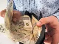 Ręce trzymają portfel z banknotami 200 zł. To symboliczne przedstawienie nagrody jubileuszowej za 15 lat pracy.
