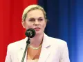 Kobieta w jasnej marynarce mówi do mikrofonu na tle czerwono-niebieskiego tła.