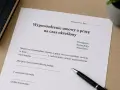 Dokument "Wypowiedzenie umowy o pracę na czas określony" leży na biurku obok długopisu i notatnika.