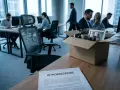 Pudełko z osobistymi rzeczami i zdjęcie pary na biurku, obok dokument "Wypowiedzenie". To symbol likwidacji stanowiska pracy.