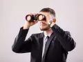 Mężczyzna w garniturze przez lornetkę szuka odpowiedzi na pytanie: wakat co to.