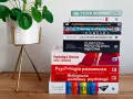 Stos książek o psychologii, od ogólnych po specjalistyczne, sugeruje, ile trwają studia psychologiczne. Obok zielona roślina.
