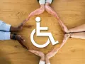 Dłonie różnych osób tworzą okrąg wokół symbolu osoby na wózku, symbolizując wsparcie dla osób z niepełnosprawnością intelektualną i innymi.