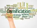Ręka pisze słowo "Gamification" otoczone chmurą powiązanych terminów, takich jak "gra", "nagroda", "bonus", "strategia", "motywacja" i "sieć". Grywalizacja w akcji!