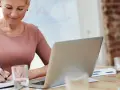 Kobieta notuje w zeszycie, pracując nad dokumentacją do centralnego rejestru umów.