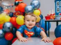 Uśmiechnięty chłopiec w stroju Supermana, otoczony balonami. Jego radość to jedna z jego mocne strony dziecka przykłady.