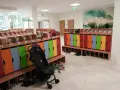 Kolorowe szafki i ławki w zespole szkolno-przedszkolnym, gotowe na przyjęcie dzieci. Wózek spacerowy czeka na swojego małego pasażera.