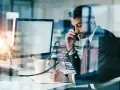 Biznesmen w garniturze rozmawia przez telefon, notując w zeszycie. Nawet w obliczu siły wyższej, praca wre.