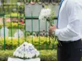 Mężczyzna w białej koszuli i niebieskim krawacie trzyma bukiet białych kwiatów i różaniec. To jego urlop okolicznościowy śmierć teścia.