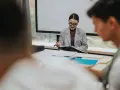 Kobieta w okularach i szarym żakiecie prowadzi prezentację. Na stole leżą dokumenty i materiały, tworząc atmosferę nauki i art 20 kn.
