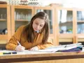 Dziewczyna pisze w zeszycie, przygotowując się do egzaminu. Marzy o stypendium szkolnym, które pomoże jej w dalszej nauce.