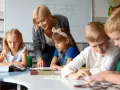 Uśmiechnięta nauczycielka wspiera dzieci w nauce. To praca, którą wykonuje oligofrenopedagog, pomagając maluchom rozwijać się.