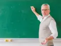 Doświadczony nauczyciel akademicki z kredą w dłoni, tłumaczy coś przy zielonej tablicy.