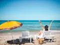 Kobieta cieszy się słońcem na plaży, w pełni wykorzystując swój urlop. Obok parasol i leżaki.