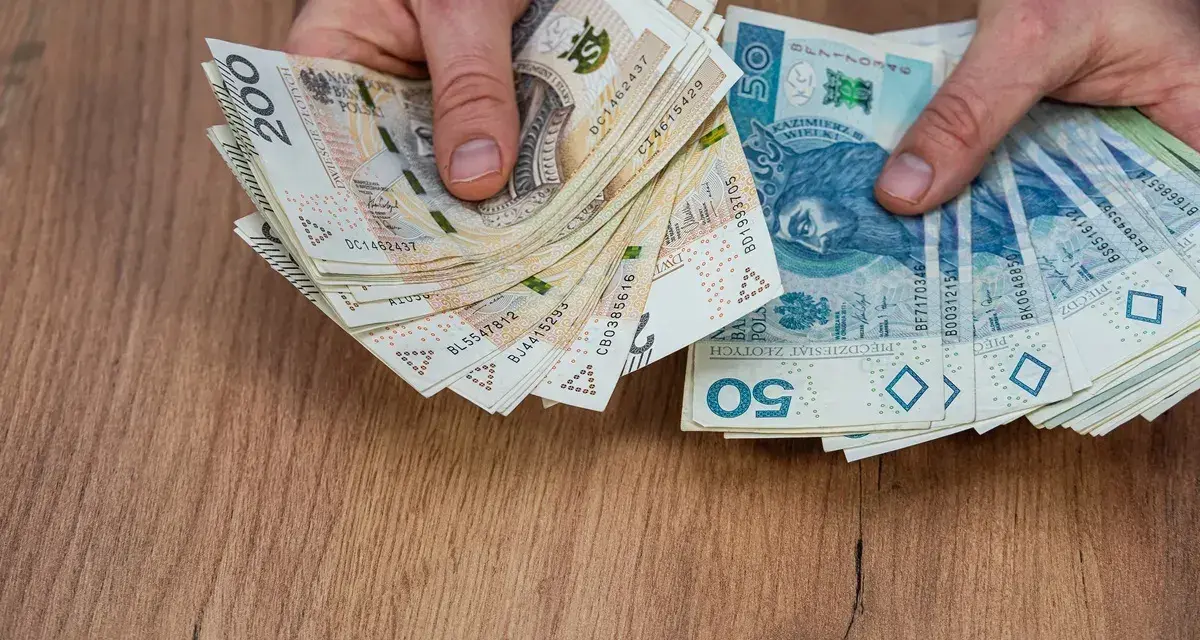 Dłonie trzymające stosy polskich banknotów 200 zł i 50 zł, być może na sześciomiesięczną odprawę emerytalną.