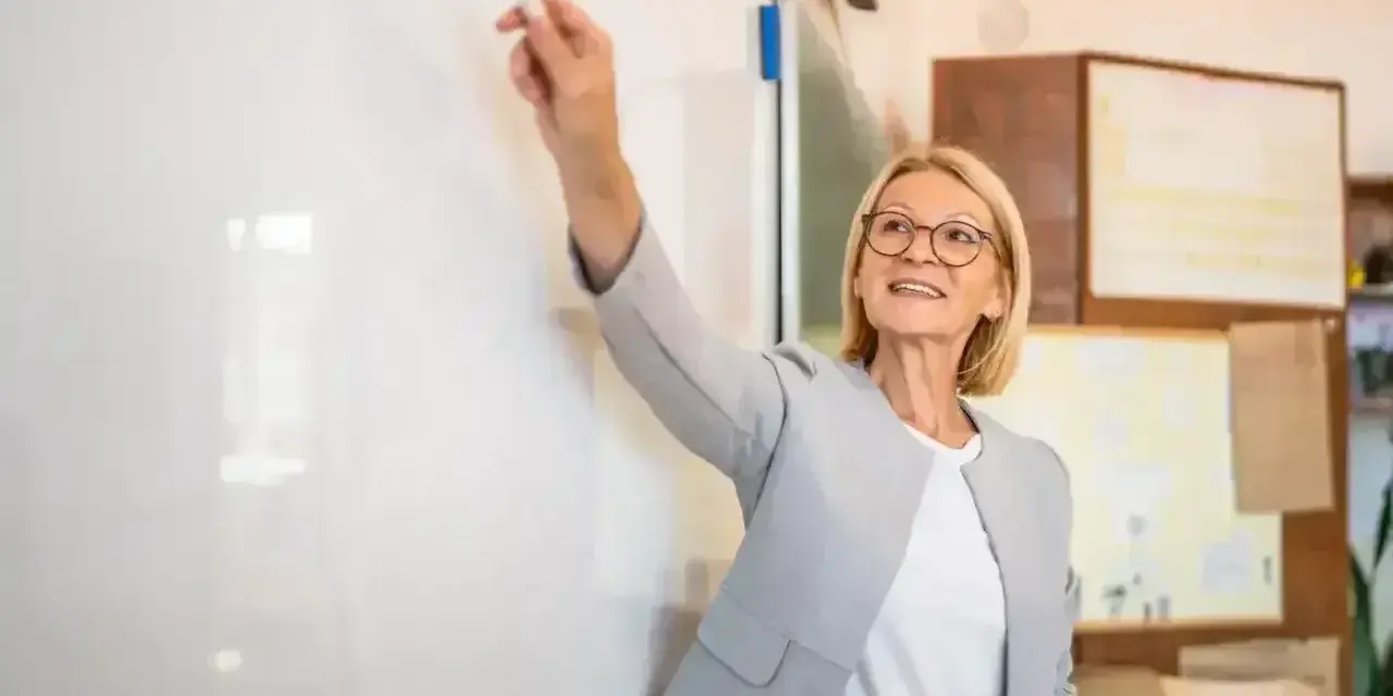 Nauczycielka z markerem przy tablicy, uśmiechnięta. To może być ocena pracy nauczyciela początkującego.