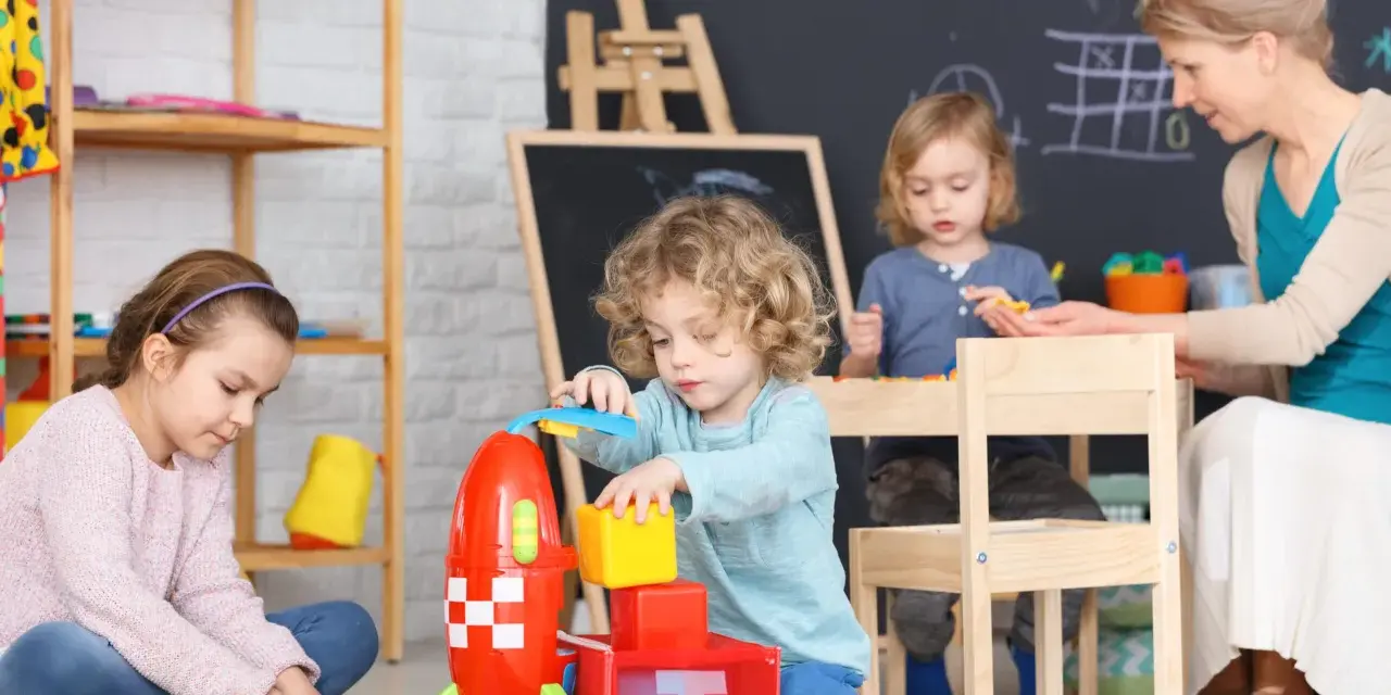 Opiekunka dziecięca z dziećmi buduje rakietę z klocków.