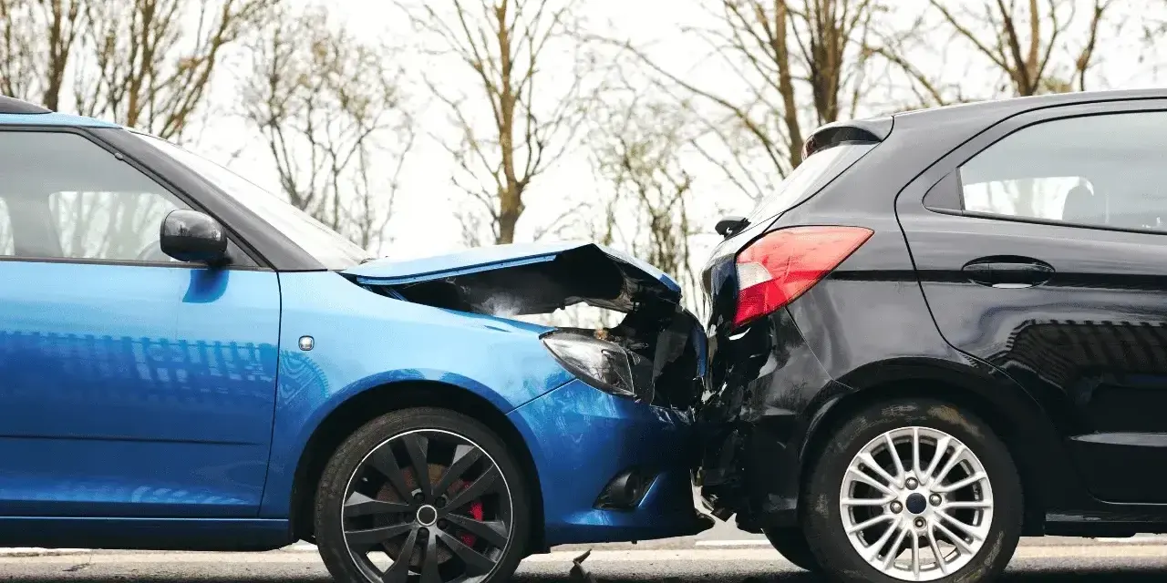 Wypadek drogowy. Niebieski i czarny samochód zderzyły się. To zdarzenie to siła wyższa, jakby kodeks pracy nie obowiązywał.