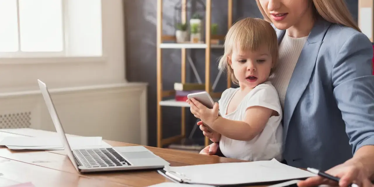 Praca na urlopie macierzyńskim? Młoda mama z dzieckiem przy biurku z laptopem i tabletem, pokazująca, że można łączyć obowiązki.