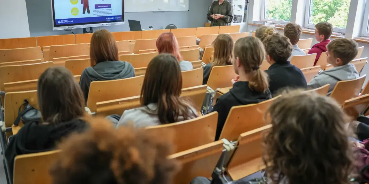 Wykład o przygotowaniu pedagogicznym dla psychologów. Studenci słuchają prelegentki przy tablicy interaktywnej.
