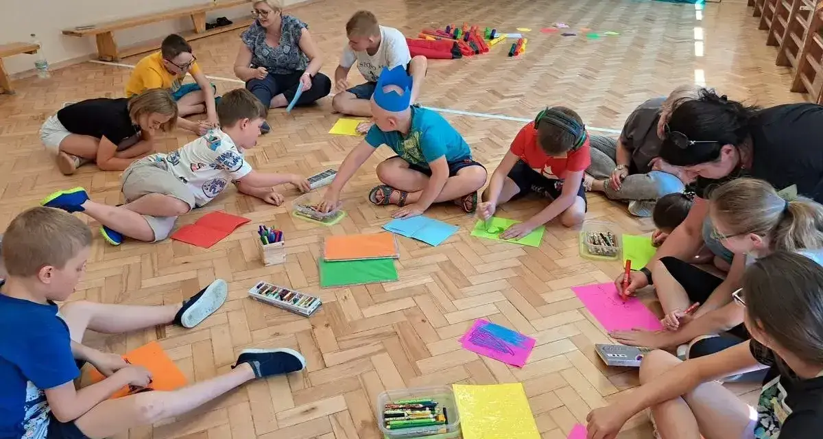 Dzieci klas 1-3 biorą udział w zabawach integracyjnych, rysując na kolorowych kartkach.