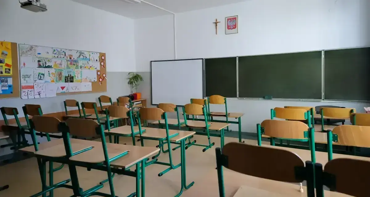 Pusta klasa szkolna z ławkami i krzesłami. Na ścianie tablica, projektor i dziecięce rysunki. Dziś odwołane zajęcia w szkołach.