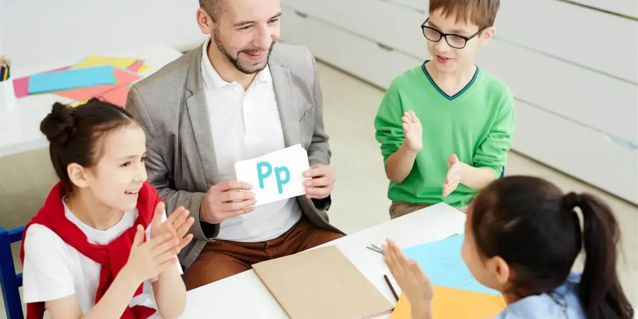 Nauczyciel pokazuje literę "Pp" podczas zebrania z rodzicami. Dzieci klaszczą, ucząc się alfabetu.