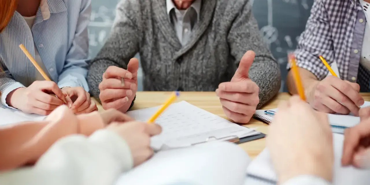 Uśmiechnięty nauczyciel w stanie nieczynnym, otoczony przez studentów piszących notatki.