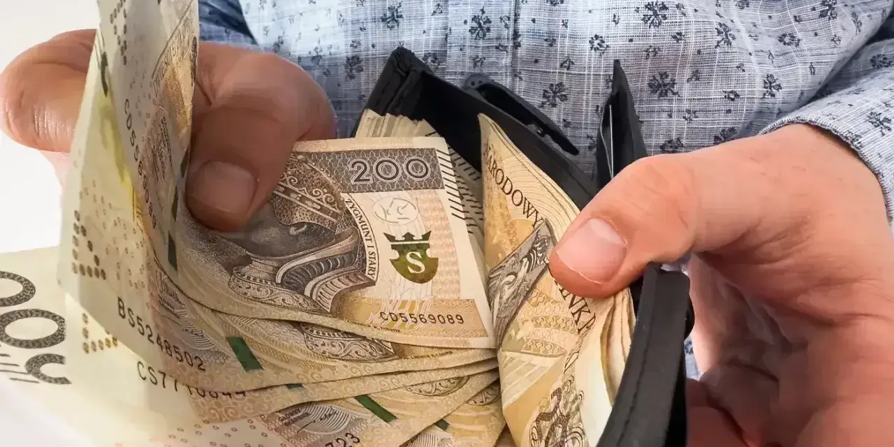 Ręce trzymają portfel z banknotami 200 zł. To symbol nagrody jubileuszowej za 40 lat pracy w budżetówce.