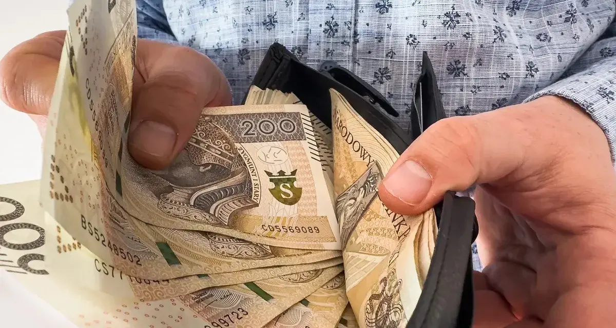 Ręce trzymają portfel z banknotami 200 zł. To symboliczne przedstawienie nagrody jubileuszowej za 15 lat pracy.